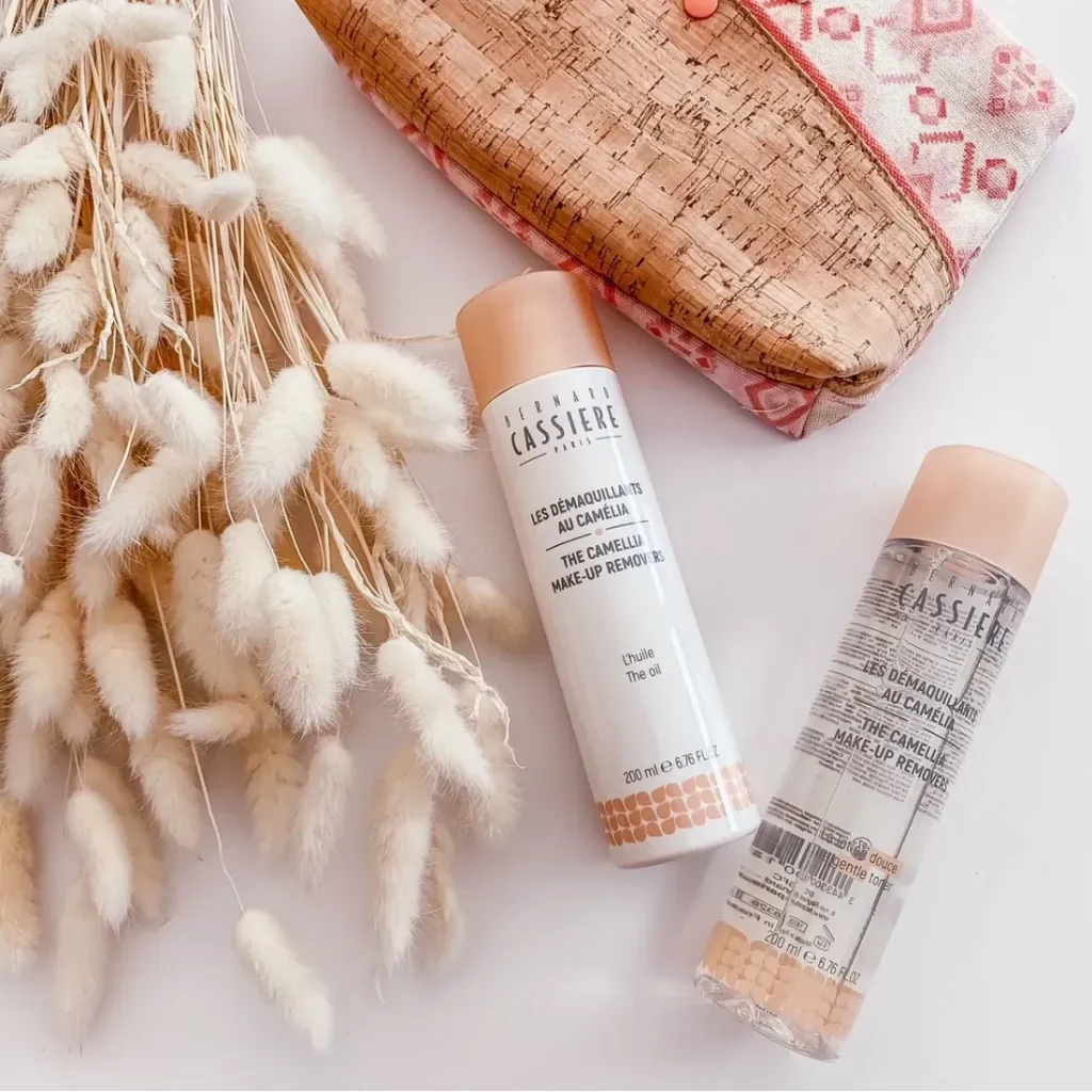 Two bottles of Bernard Cassiere the oil cleanser and the gentle toner styled in a flat lay with dried bunny tail grass and a cork pouch on a white background.