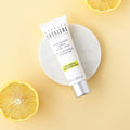 A squeeze tube of Bernard Cassiere lemon mattifying moisture fluid set on a small white round plate, styled with lemon slices on a pale yellow background.