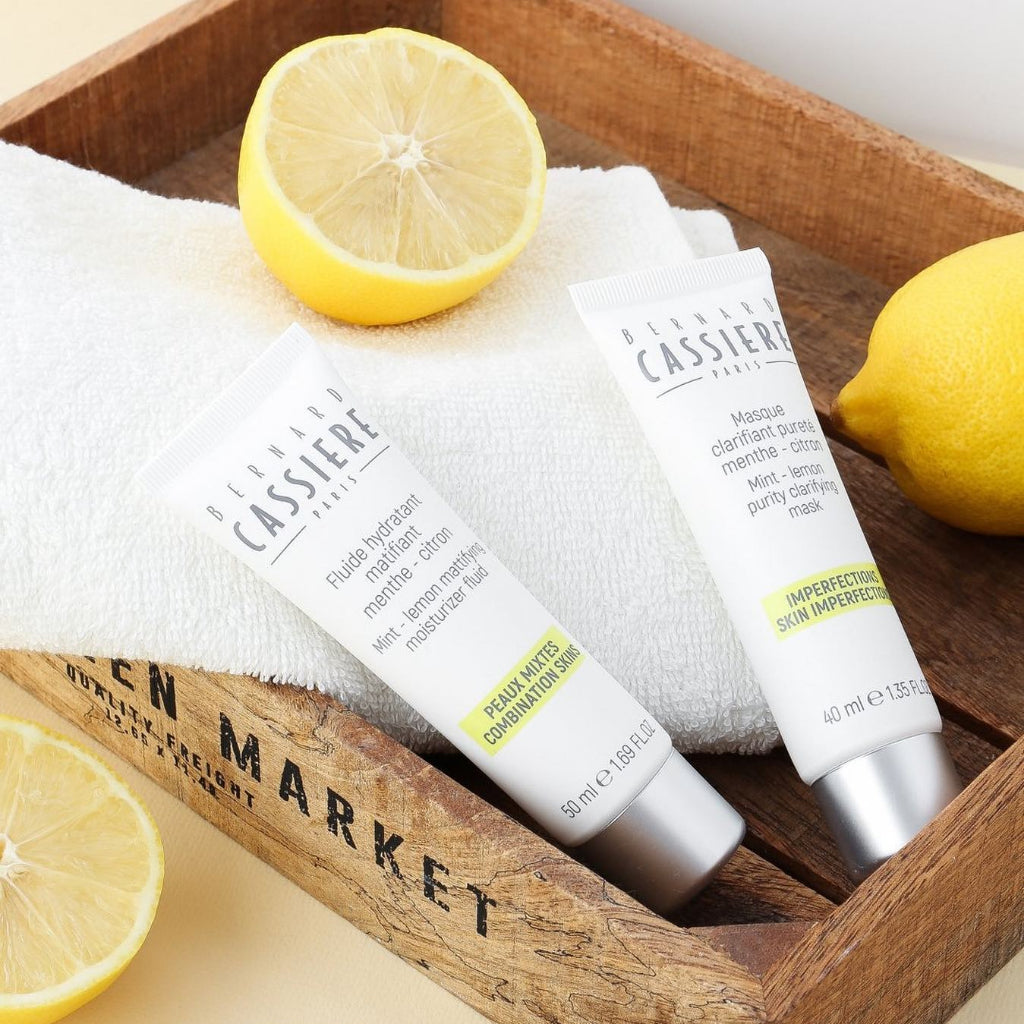 Two tubes of Bernard Cassiere Paris skincare cream and mask arranged in a rustic wooden crate with lemon halves and a white towel.