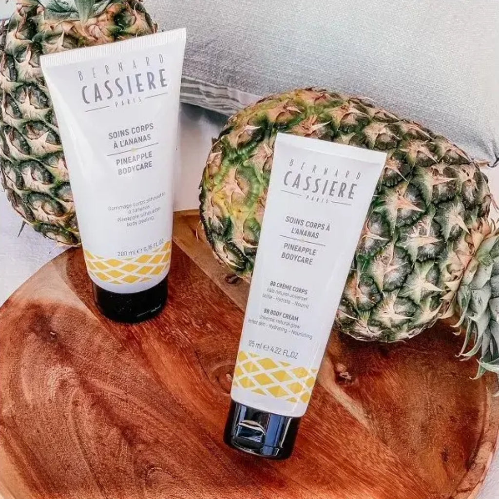 Two tubes of Bernard Cassiere pineapple slimming body products displayed on a wooden tray with pineapples in the background