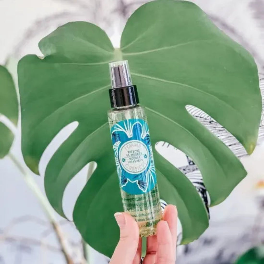 A hand holding a bottle of the Bernard Cassiere multi-purpose oil enhancer in front of a large green monstera leaf.