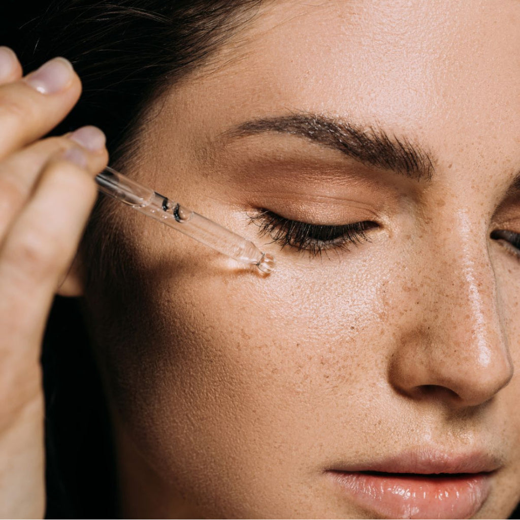 Close-up of a woman applying a dropper of bernard cassiere custom- made moisturizing serum to her face.