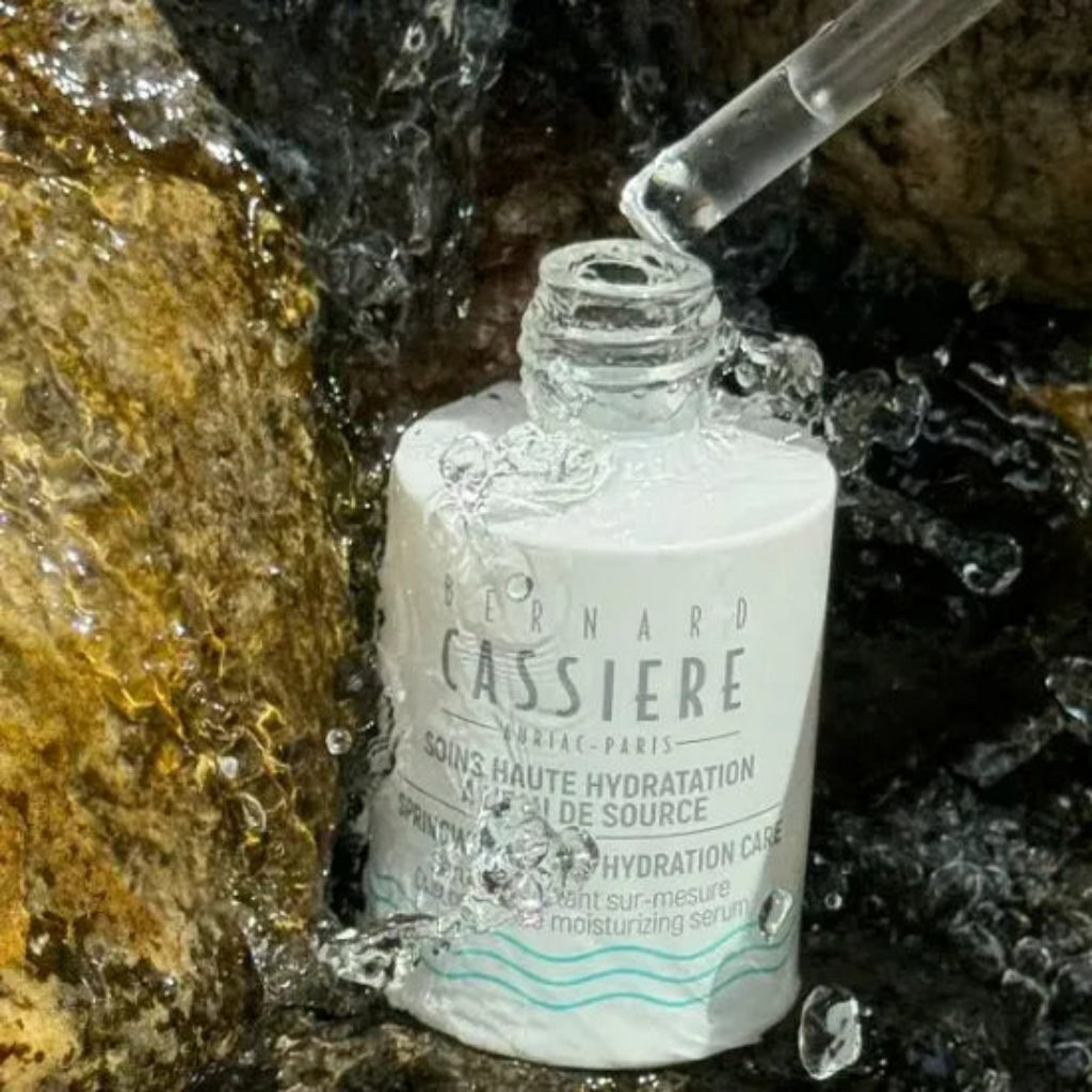 Bernard Cassiere Springwater Hydration Care moisturizing serum in a  glass bottle with a white label, shown with a glass dropper above the open bottle, surrounded by splashing water and rocks.