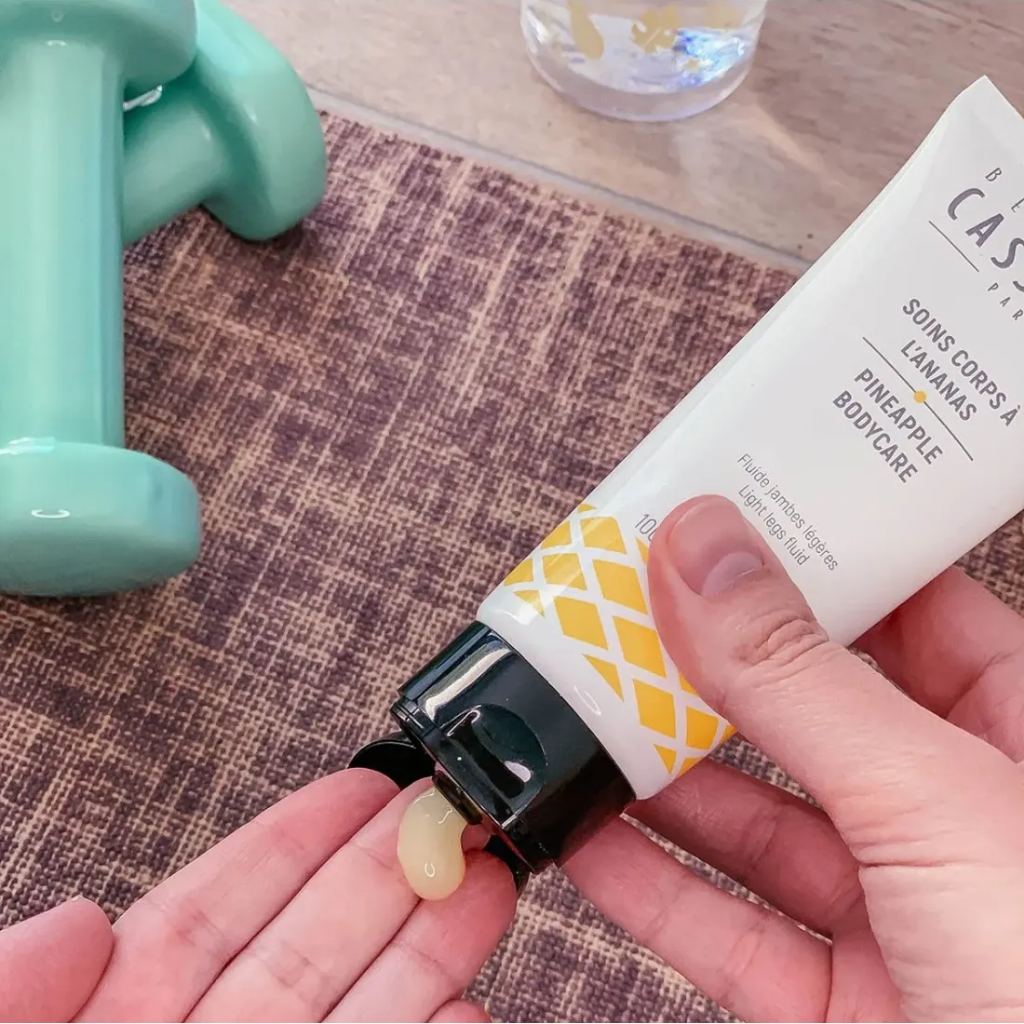 A person squeezing out the Bernard Cassiere pineapple body care light legs fluid onto their hand revealing a light yellow gel with weights in the background. 