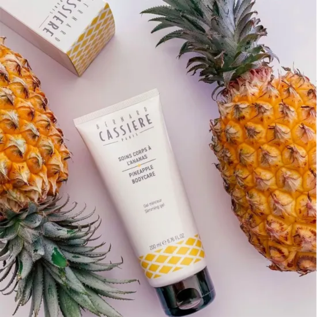 A tube of Bernard Cassiere Paris Pineapple Bodycare slimming gel is displayed diagonally between two whole pineapples on a light pink background, with a branded box partially visible in the top left.